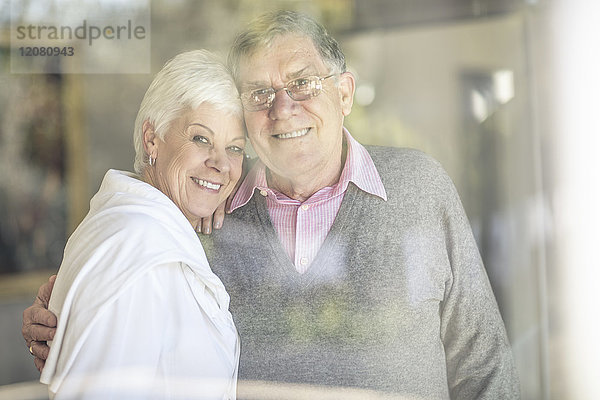Porträt eines lächelnden Seniorenpaares hinter der Fensterscheibe