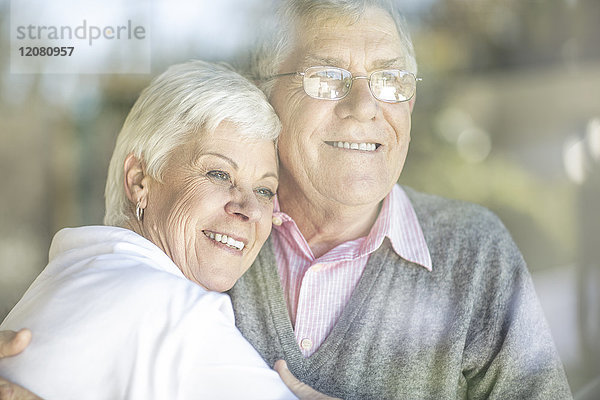 Porträt eines lächelnden Seniorenpaares hinter der Fensterscheibe