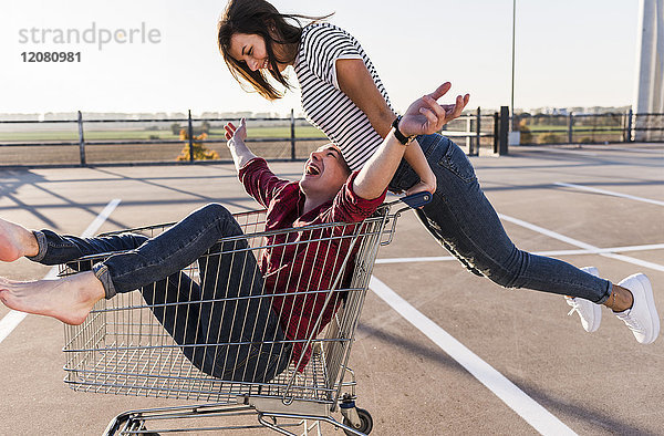 Verspieltes junges Paar mit Einkaufswagen auf Parkebene