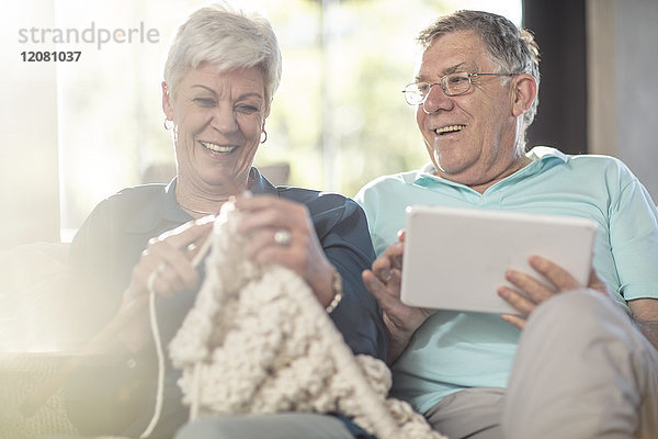 Glückliches Seniorenpaar auf der Couch zu Hause beim Stricken und Tablettieren