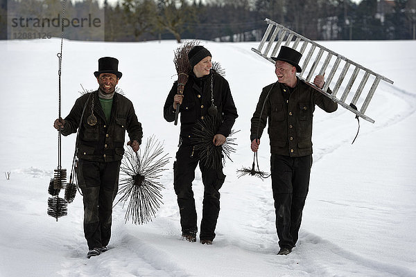 Drei lachende Schornsteinfeger im Schnee unterwegs