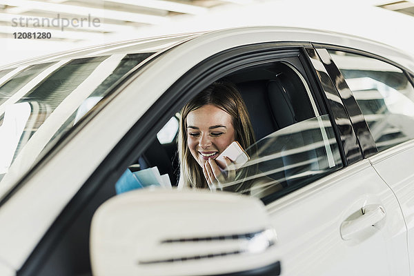 Lächelnde junge Frau mit Handy im Auto