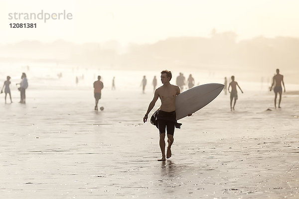 Indonesien  Bali  Surfer mit Surfbrett am Strand bei Sonnenuntergang