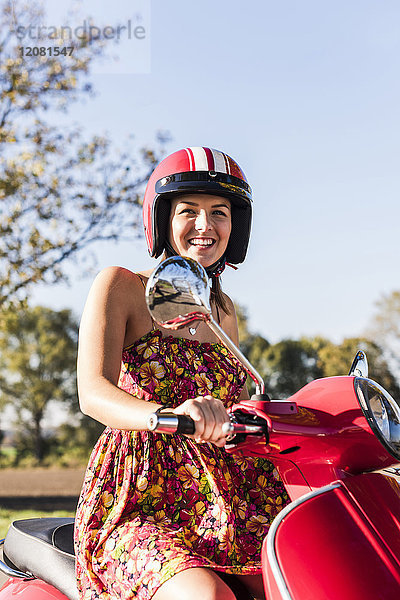 Porträt der glücklichen jungen Frau auf dem Motorroller