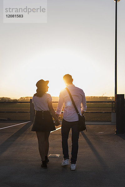 Junges Paar geht Hand in Hand auf Parkdeck bei Sonnenuntergang