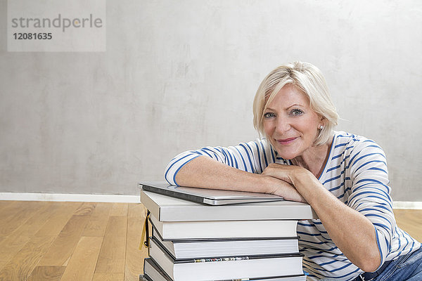 Porträt einer lächelnden älteren Frau  die sich auf einen Stapel Bücher und einen Laptop stützt.