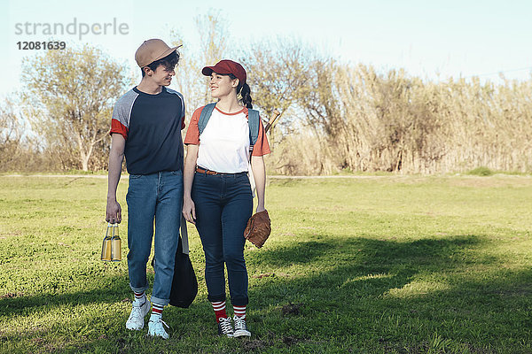 Lächelndes junges Paar mit Baseballausrüstung beim Spaziergang im Park