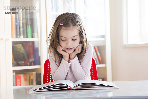Porträt des kleinen Mädchens am Tisch beim Lesen eines Buches