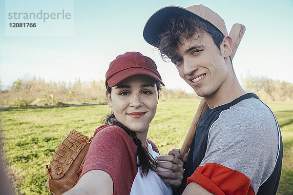 Porträt eines lächelnden jungen Paares mit Baseballausrüstung im Park
