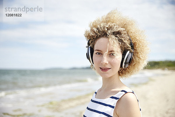 Portrait einer jungen blonden Frau mit Kopfhörer am Strand