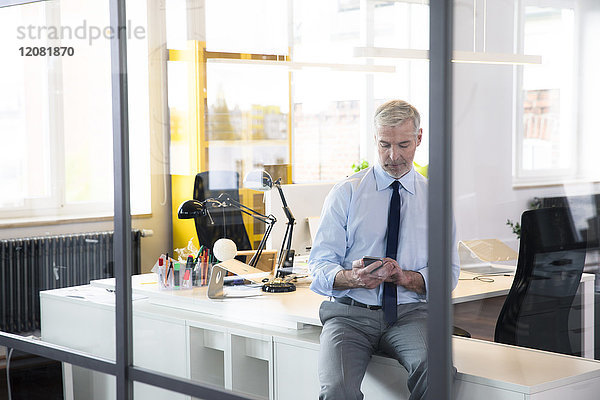 Geschäftsmann sitzend im Büro  mit Smartphone  Nachrichten lesen