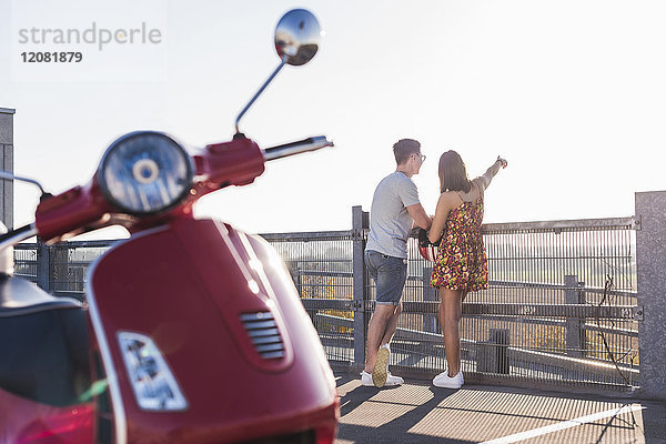 Junges Paar auf Parkebene stehend mit Motorroller im Vordergrund