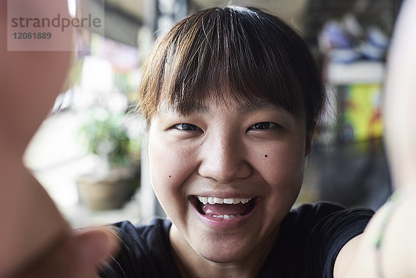 Porträt einer lachenden Frau  die sich selbst mit dem Smartphone fotografiert.