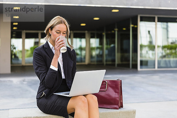 Geschäftsfrau mit modischer Ledertasche und Kaffee zum Sitzen auf der Bank mit Blick auf den Laptop