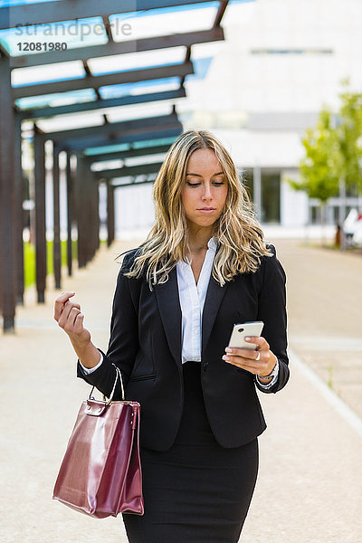 Geschäftsfrau mit modischer Ledertasche beim Blick aufs Handy