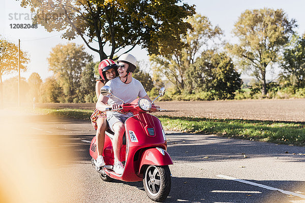 Fröhliches junges Paar beim Motorrollerfahren auf der Landstraße
