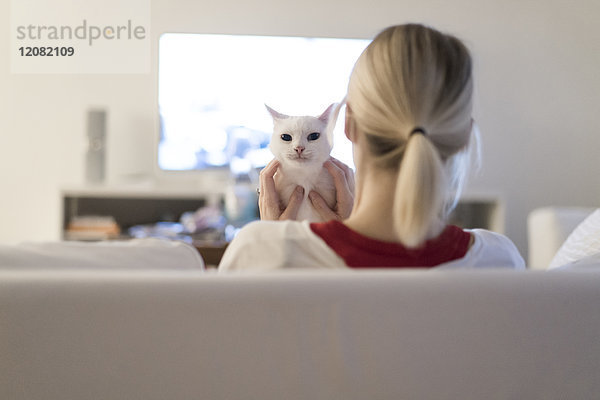 Frau sitzt mit ihrer Katze auf der Couch und schaut fern.