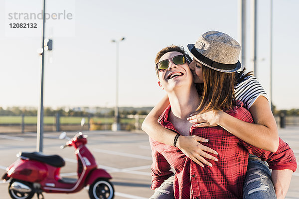 Fröhliches junges Paar auf Parkebene mit Motorroller im Hintergrund