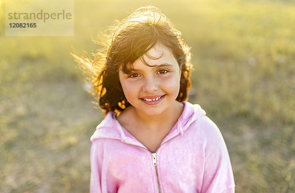 Porträt eines lächelnden kleinen Mädchens mit blasenden Haaren im Gegenlicht