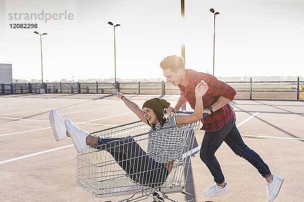 Verspieltes junges Paar mit Einkaufswagen auf Parkebene