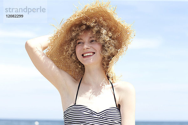 Porträt einer glücklichen jungen Frau mit Strohhut am Strand
