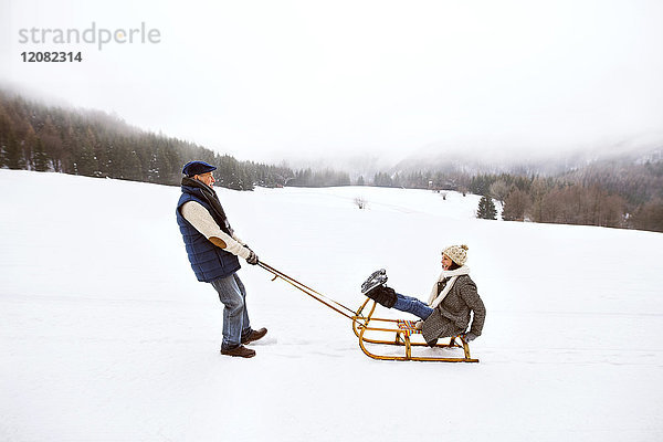 Seniorenpaar beim Schlittenfahren in verschneiter Landschaft