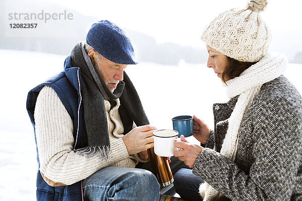 Seniorenpaar bei einer Pause mit heißen Getränken im Schnee
