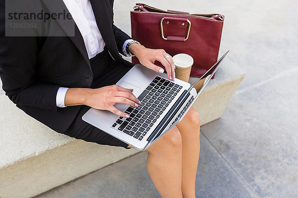 Geschäftsfrau mit modischer Ledertasche und Kaffee zum Sitzen auf der Bank mit Laptop  Teilansicht