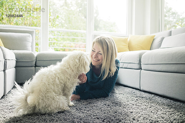 Lächelnde Frau streichelt ihren Hund im Wohnzimmer
