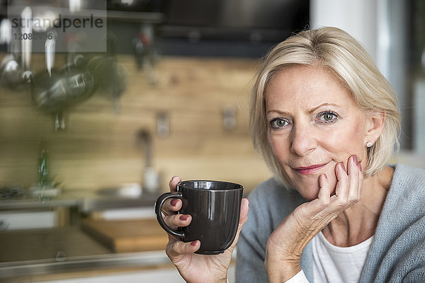 Porträt der lächelnden Seniorin mit Kaffeetasse in der Küche