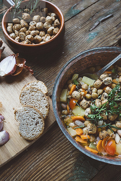 Mediterrane Suppe im Kupfertopf  Schüssel mit Croutons und Brotscheiben auf Holzplatte