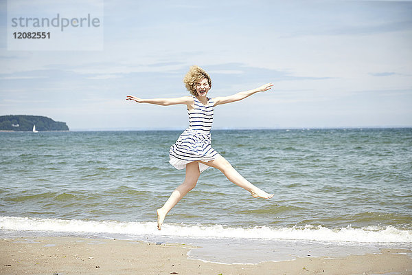 Fröhliche junge Frau  die vor dem Meer in die Luft springt.