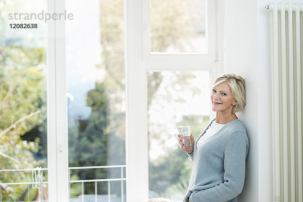 Porträt einer älteren Frau mit Wasserglas vor dem Fenster