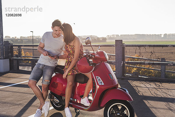 Glückliches junges Paar auf Parkebene mit Motorroller und Handy