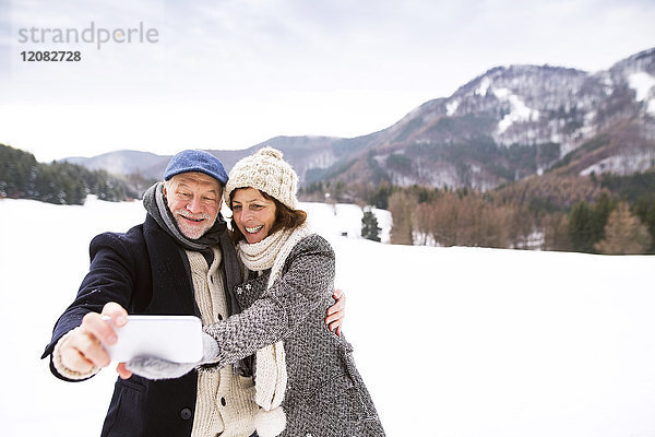 Seniorenpaar beim Küssen mit dem Handy in der Winterlandschaft