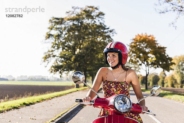 Glückliche junge Frau auf dem Motorroller auf der Landstraße