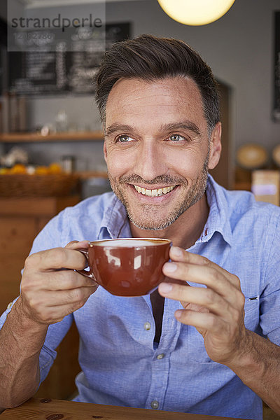 Porträt eines lachenden Mannes mit Tasse Kaffee in einem Coffee Shop