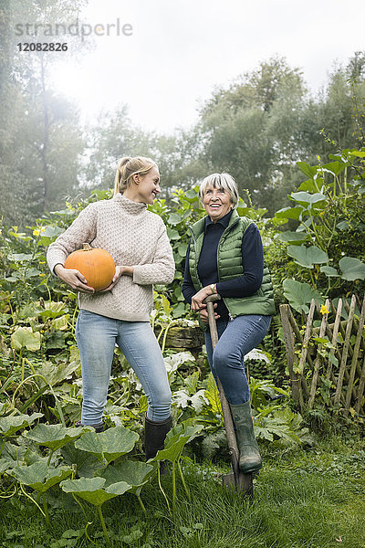 Glückliche junge Frau mit ihrer Großmutter hält Kürbis im Garten