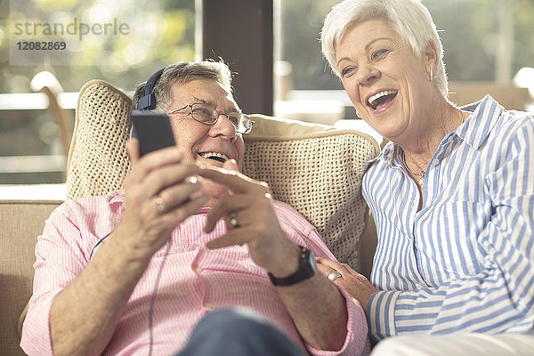 Glückliches Seniorenpaar mit Handy und Kopfhörer auf der Couch zu Hause