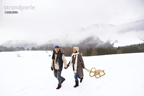 Glückliches Seniorenpaar mit Schlittenwanderung in verschneiter Landschaft