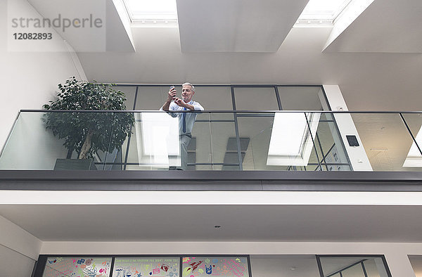 Erfolgreicher Geschäftsmann am Geländer in seinem Büro mit Smartphone