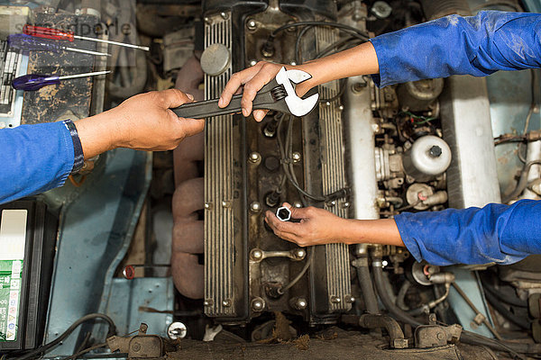 Draufsicht auf die Hände des Automechanikers und den Motor des Autos in der Reparaturwerkstatt