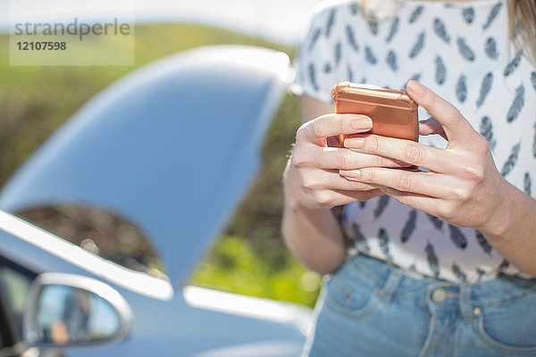 Junge Frau neben einem liegengebliebenen Auto  mit Smartphone  Mittelteil