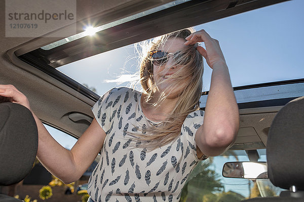 Junge Frau im Auto  die aus dem offenen Schiebedach schaut