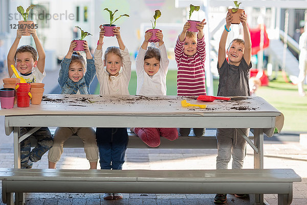 Mädchen und Jungen in der Vorschule  Porträt  das Topfpflanzen am Picknicktisch hochhält