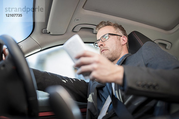 Geschäftsmann beim Autofahren  Smartphone in der Hand  niedriger Blickwinkel