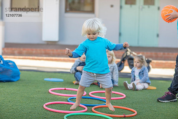 Mädchen in der Vorschule  das im Garten über Plastikkörbe springt