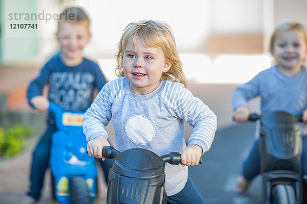 Mädchen und Jungen in der Vorschule  Motorradrennen schieben Motorräder im Garten