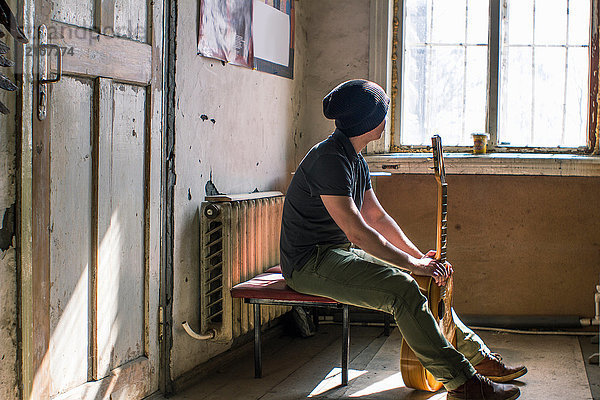 Junger Mann auf Stuhl sitzend  Gitarre haltend