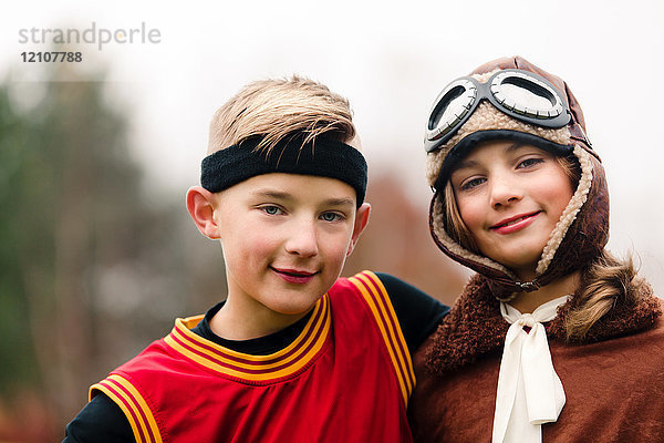 Porträt eines Jungen und einer Zwillingsschwester in Basketball- und Pilotenkostümen zu Halloween